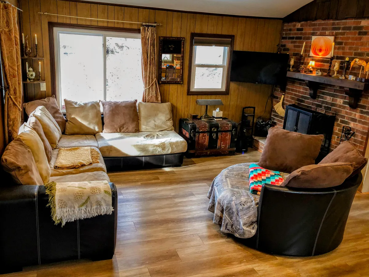 This image depicts a cozy living room featuring a plush sofa set, a wooden coffee table, and a striking brick fireplace adorned with a colorful blanket. The overall setting feels inviting and is perfect for relaxing, socializing, or enjoying movie nights.