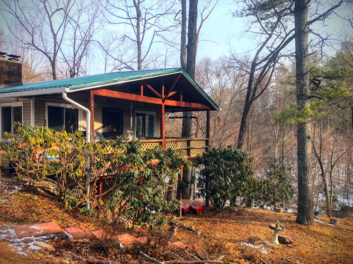 A charming wooden porch with a green roof, surrounded by lush greenery. The porch invites relaxation, offering a tranquil space to enjoy a morning coffee or quiet moments after a day out. The natural setting emphasizes the cabin's seclusion and connection to the outdoors.